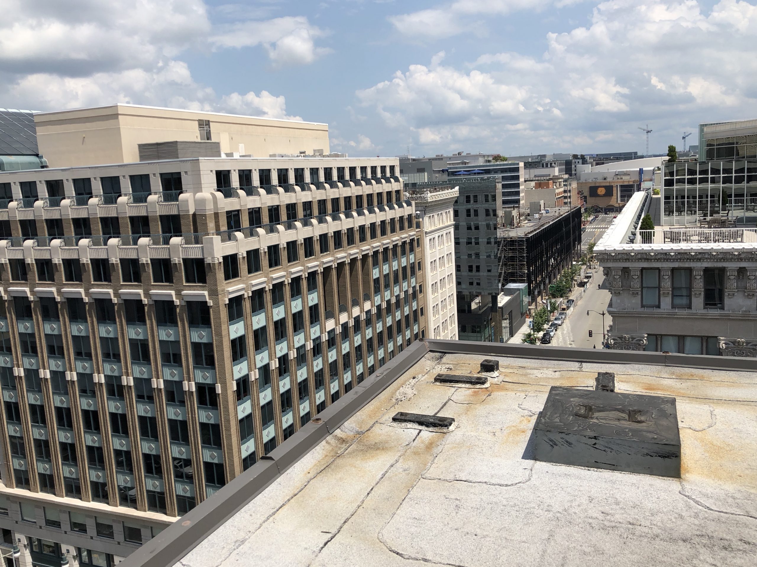 Flat commercial roof with a perimeter parapet and roof hatch overlooking an office building