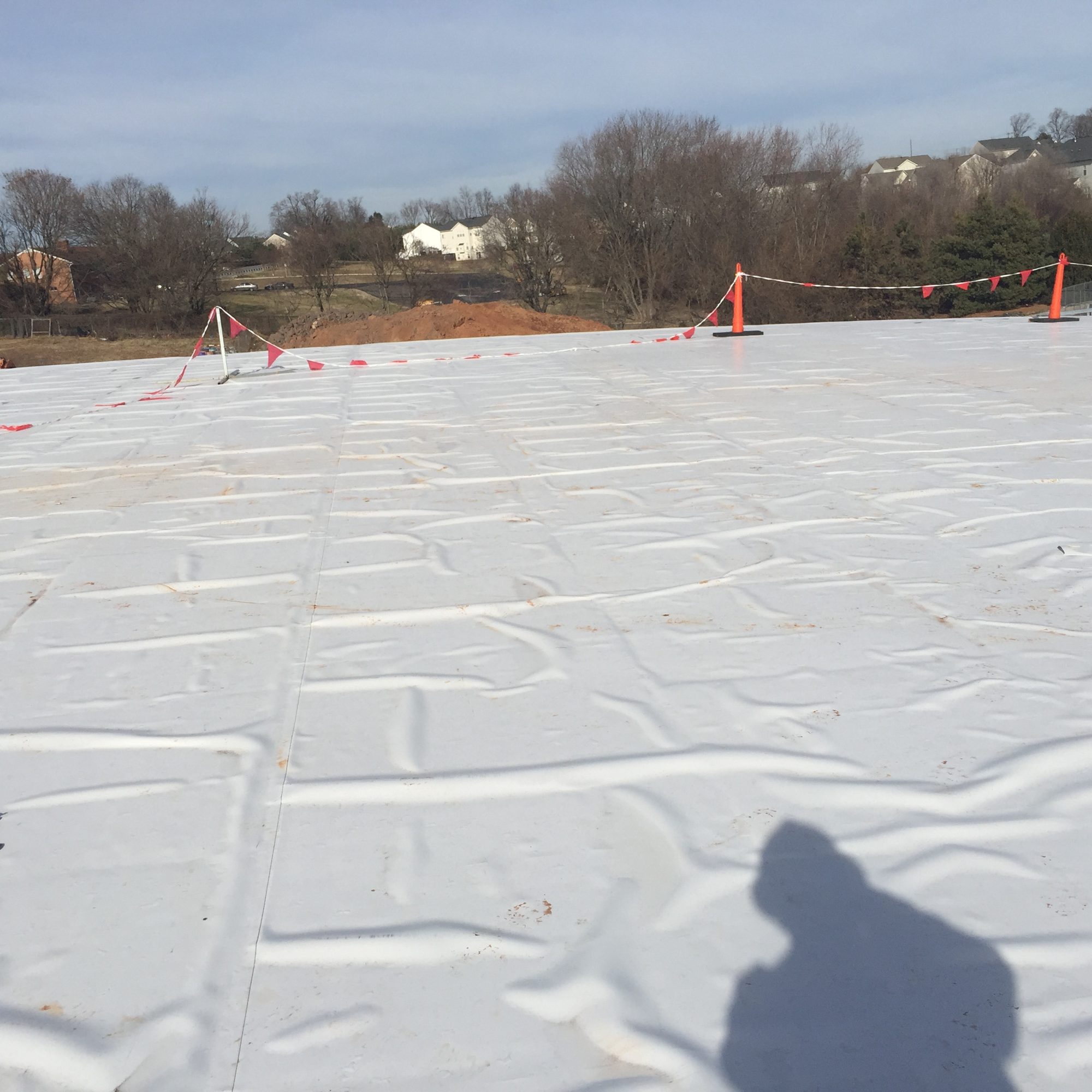 Newly installed white single-ply membrane roof with safety flag line and cones at the roof edge
